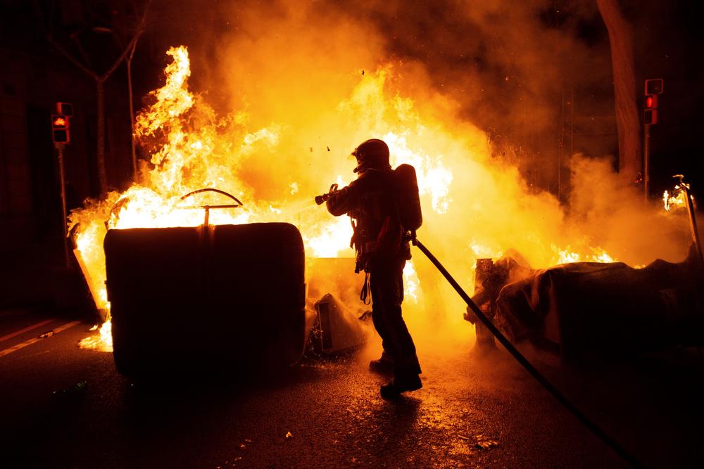 Un integrante del cuerpo de Bomberos intenta sofocar un fuego en unos contenedores   / ENRIC FONTCUBERTA